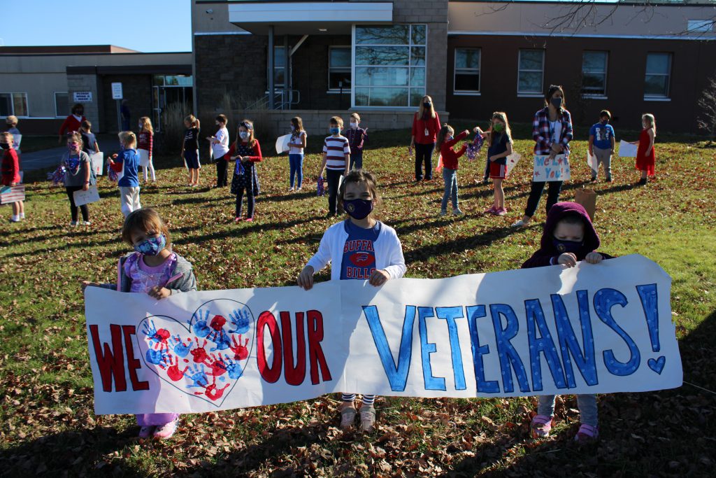 elementary students hold up signs in front of the school