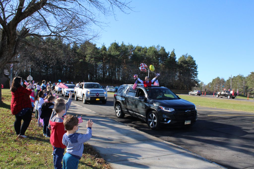 a person stands up in a vehicle through a sunroof while holding balloons in a school parking lot