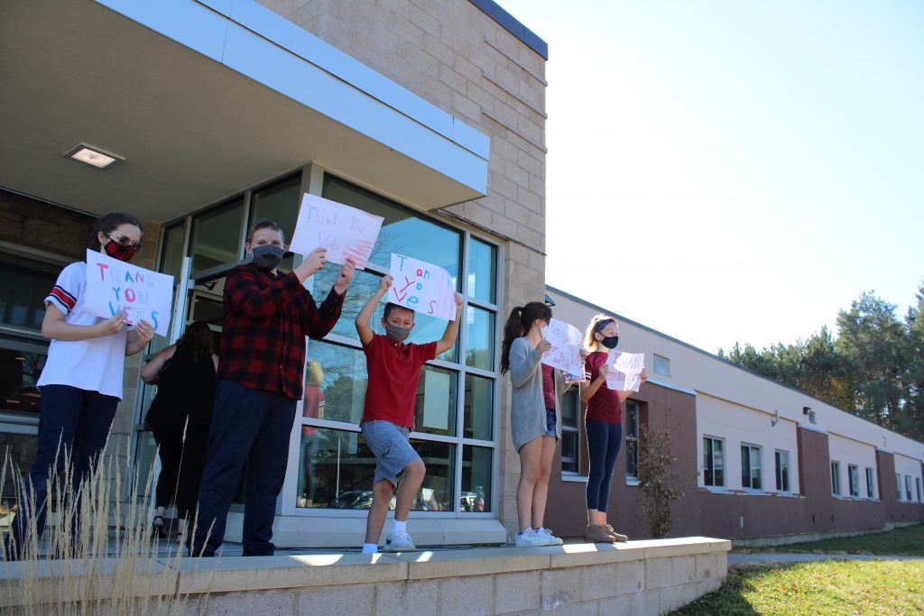 elementary students hold up signs in front of the school