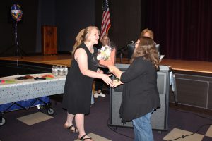 a woman with blonde hair and a black dress accepts flowers and a balloon from a woman with brown hair