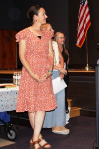a woman wearing a coral colored dress stands in an auditorium