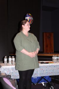 a woman wearing a green top and black pants poses in front of a table