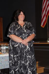 a woman wearing a black and white dress smiles standing in front of a theatrical stage