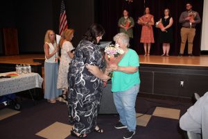 a woman wearing a black and white dress accepts flowers and a balloon from a short woman with white hair