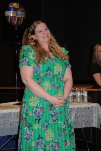a woman wearing a green floral dress smiles while standing in front of a table