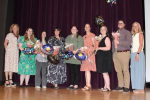 men and women pose together on a theatrical stage with several of them holding balloons and flowers