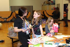 a young woman holds a clipboard while she talks to an elementary student