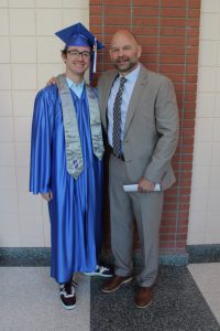 a student wearing a blue cap and gown poses with a teacher