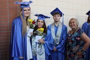 three students in caps and gowns pose next to a woman in a hallway