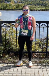 a woman wearing a tank top and black yoga pants wears sunglasses and a ribbon around her neck as she poses outside near a river