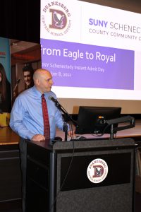 a man wearing a blue shirt and a red tie speaks into a microphone