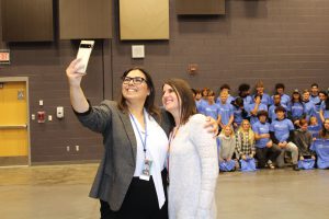 two women take a selfie with a group of students standing behind them