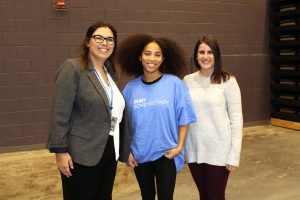 two adult women stand next to a young female student who is wearing a blue t-shirt.