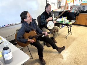 a woman laughs as she plays the guitar next to a man playing a banjo