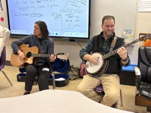 a woman plays a guitar and a man plays a banjo in a school classroom
