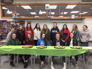 students pose behind table full of cookies