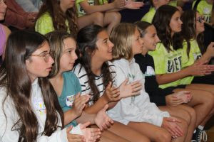 a group of young students sit in a gymnasium for an assembly