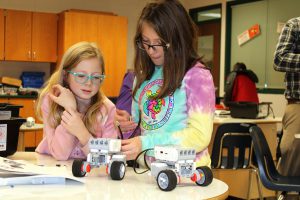 two young girls work on a project to build a robot