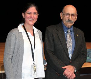 a younger woman stands next to an older gentleman in front of a theatrical stage