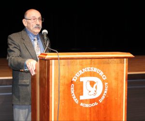 an older gentleman speaks into a microphone at a podium