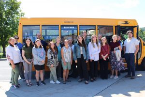 a group of teachers stands outside in front of a school bus