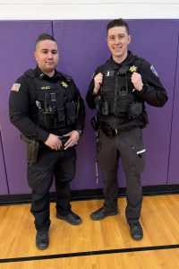 two police officers pose against a purple wall
