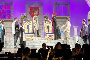 student actors dressed as royalty act out a scene with a stage set that looks like a castle 
