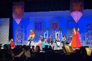 student actors act out a scene on stage with blue lighting on the set