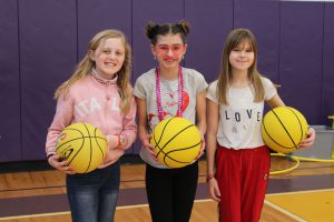 three young girls hold yellow basketballs