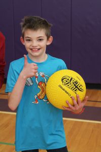a boy wearing a blue t-shirt holds a yellow ball and shows a thumbs up