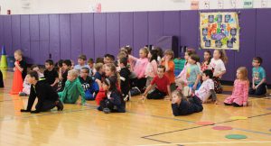 students sit on a gymnasium floor and listen to instructions