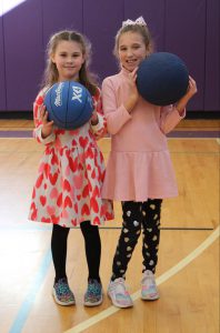 two young girls wearing dresses hold blue bouncy balls
