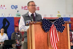 a man wearing glasses and a tie speaks into a microphone on a podium