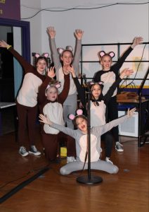 six young students pose behind a microphone while dressed up as rats