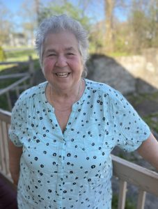 a woman with white hair poses outside on a deck