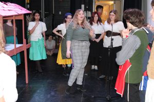 a woman gives directions to a play cast on a theatrical stage