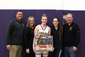 a girl holding a photo, wearing a basketball jersey, poses with three adults and another teenaged girl