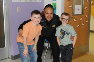 a female police officer poses with two male elementary students