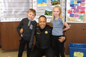 a female police officer poses with a boy and girl in a classroom