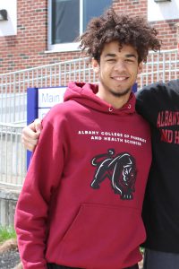 a teenaged boy wears a crimson hooded sweatshirt outside of a school