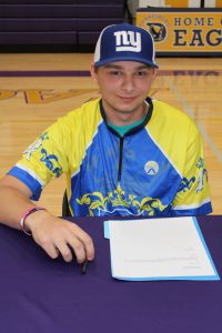 a young man wearing a yellow and blue hersey and a baseball cap sits at a table in a gymnasium