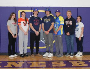 students pose in front of a purple wall in a gymnasium