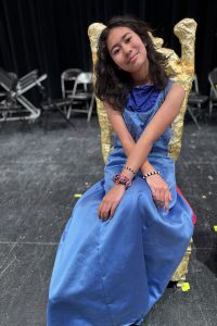 a young girl sits in a royal chair wearing a long blue dress