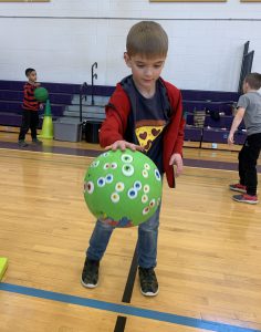 a young boy bounces a green ball in a gymnasium