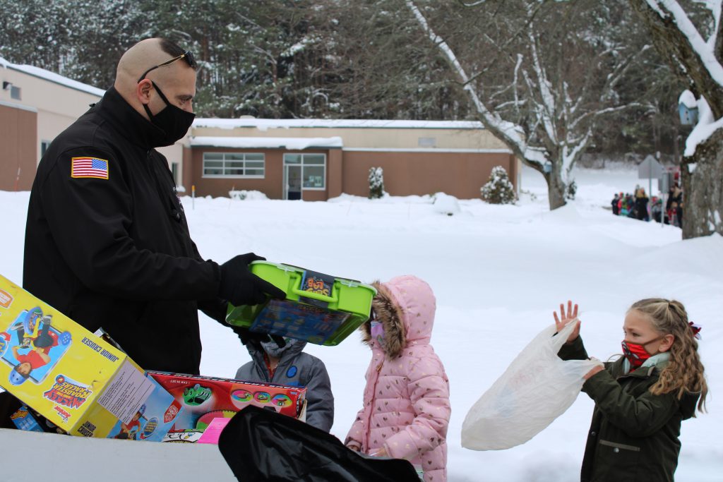 a sheriff's deputy gives an unwrapped gift to an elementary student outside of a school