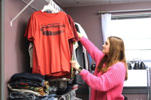 a young girl in a pink sweater hangs up an orange t-shirt on a hanger