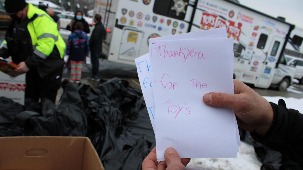 a school resource officer holds up handwritten thank you cards that say "thank you for the toys