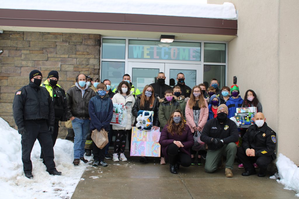 a sixth grade class poses with their teacher and a group of first responders outside of an elementary school