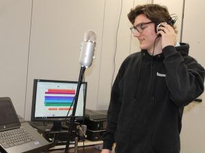 a high school student holds headphones to their ear and sings in a mock recording studio in a high school classroom