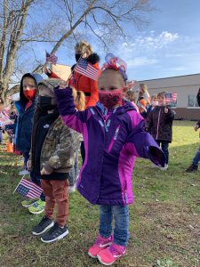 a young girl wearing a purple coat waves an American flag